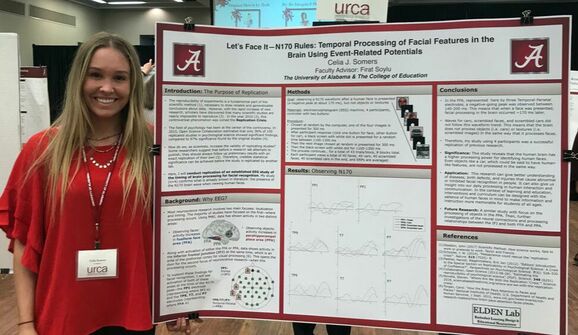 Celia Somers poses at the URCA with her research presentation poster titled "Let's Face It - N170 Rules: Temporal Processing of Facial Features in the Brain Using Event-Related Potentials."